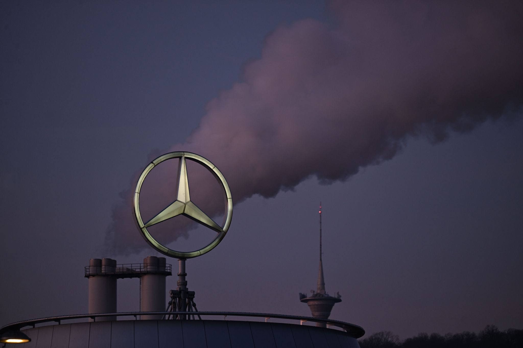 The Mercedes star, the logo of the vehicle manufacturer Mercedes-Benz, stands on a branch building, with a cloud rising from a chimney behind it.