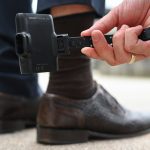 A man holds an electronic monitoring device, known as an electronic anklet, for demonstration purposes.