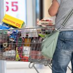 A person stands next to a full shopping cart.