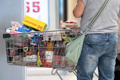 A person stands next to a full shopping cart.