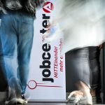 People walk past the logo of the JobCenter Berlin-Mitte at the job fair.