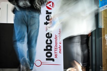 People walk past the logo of the JobCenter Berlin-Mitte at the job fair.