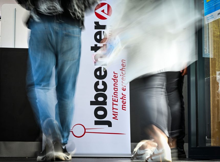People walk past the logo of the JobCenter Berlin-Mitte at the job fair.