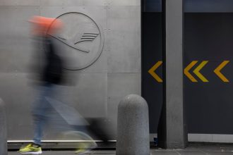 29 September 2025, Hesse, Frankfurt/Main: A man walks in front of a Lufthansa logo at Frankfurt Airport. Company sources have revealed that the Group intends to cut a fifth of its administrative jobs in the coming years. The Executive Board intends to present its comprehensive plans for staff cuts in more detail this Monday. Photo: Hannes P. Albert/dpa