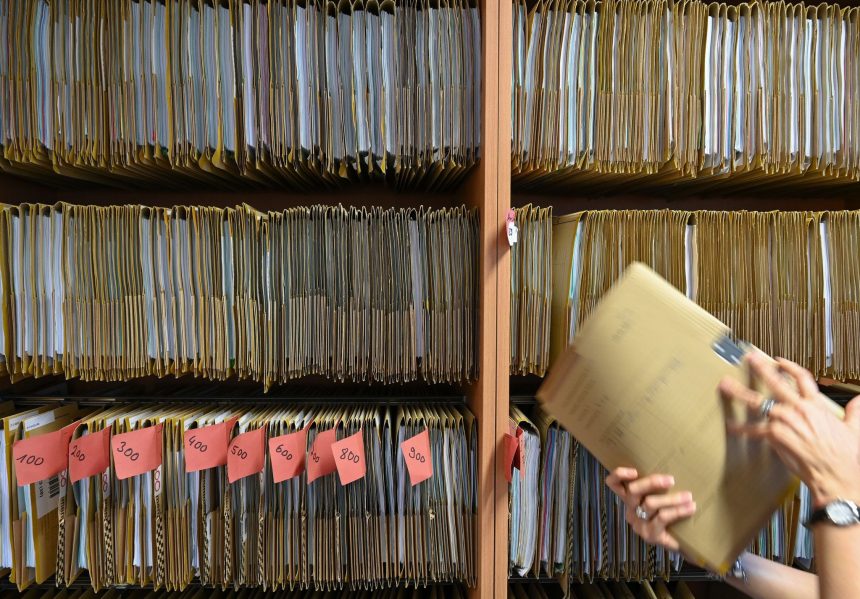 An employee of a public authority reaches for a file on a shelf. Photo: Arne Dedert/dpa