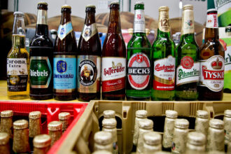13 October 2015, Bavaria, Nuremberg: Beer bottles of the Anheuser-Busch Inbev group of the brands (L-R) Corona, Diebels, Loewenbraeu, Franziskaner, Hasseroeder, Beck's and Budweiser stand next to bottles of the Pilsner Urquell and Tyskie brands of the SABMiller group in Nuremberg. Decades after a legal dispute over the beer brands Bud and Bit, the world's largest brewing group, AB InBev, is bringing its lager beer back to the German market under the name Anheuser-Busch Bud. Photo: picture alliance / Daniel Karmann/dpa