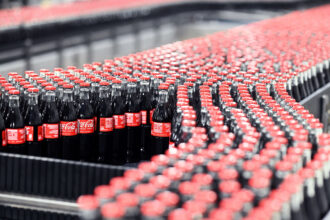 Coca-Cola glass bottles are transported on a conveyor belt at the Mannheim production site of Coca-Cola Europacific Partners - CCEP Deutschland GmbH. Photo: Uli Deck/dpa