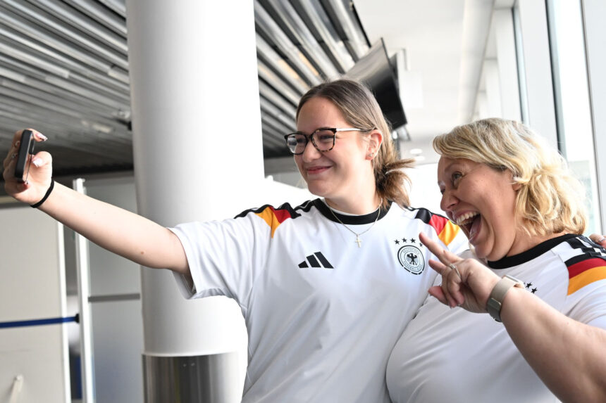 02 June 2026, Hesse, Frankfurt/Main: German football fans Leonie (L) and Anja Michalek pose for a photo with German national team shirts at Frankfurt Airport. The two passengers are flying to Chicago on the same aircraft as the German men's national football team and were presented with the shirts by the airline at the departure gate. Photo: Federico Gambarini/dpa - IMPORTANT NOTE: In accordance with the regulations of the DFL German Football League and the DFB German Football Association, it is prohibited to utilize or have utilized photographs taken in the stadium and/or of the match in the form of sequential images and/or video-like photo series.