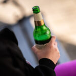 A teenager holds a bottle of beer in her hand in front of her house. Photo: Silas Stein/dpa