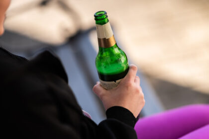 A teenager holds a bottle of beer in her hand in front of her house. Photo: Silas Stein/dpa