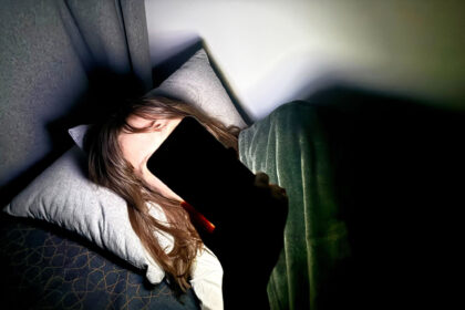 File Photo - A woman lies on a bed and holds a smartphone in front of her face. Photo: Alicia Windzio/-/dpa