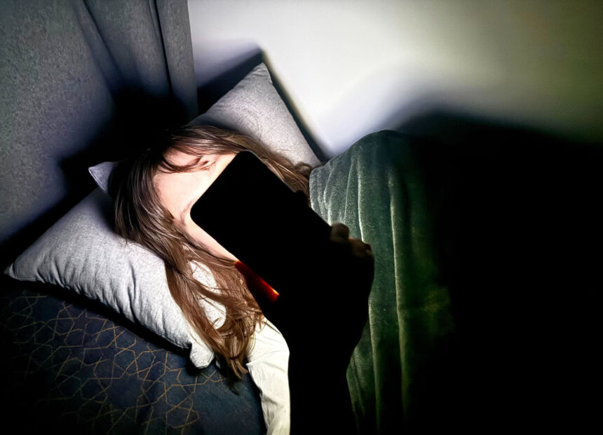 File Photo - A woman lies on a bed and holds a smartphone in front of her face. Photo: Alicia Windzio/-/dpa