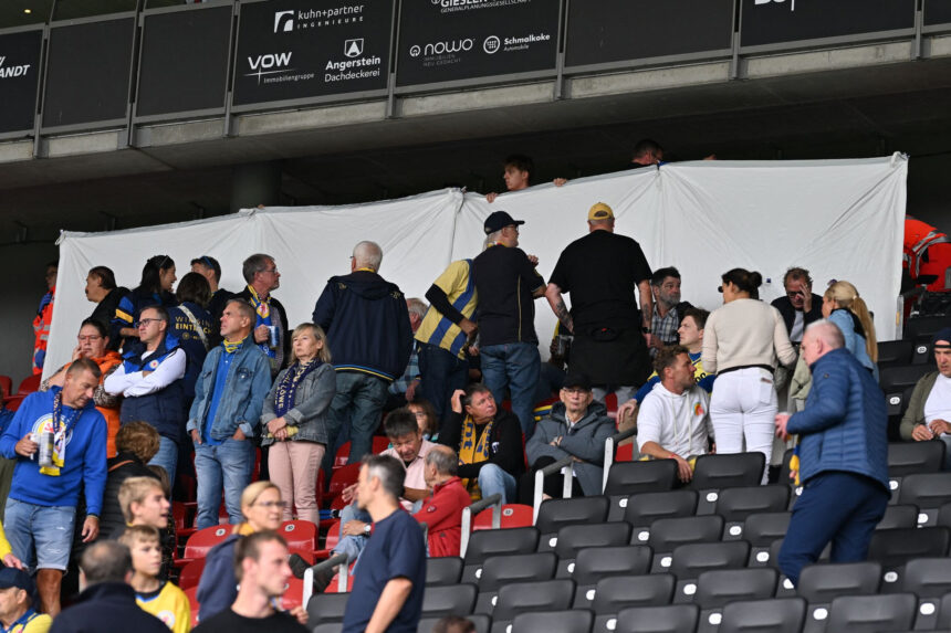 A white sheet has been stretched out due to an emergency medical response as spectators stand and sit in the stands during the German 2nd Bundesliga soccer match between Eintracht Braunschweig and SG Dynamo Dresden at Eintracht Stadium. Photo: Swen Pförtner/dpa